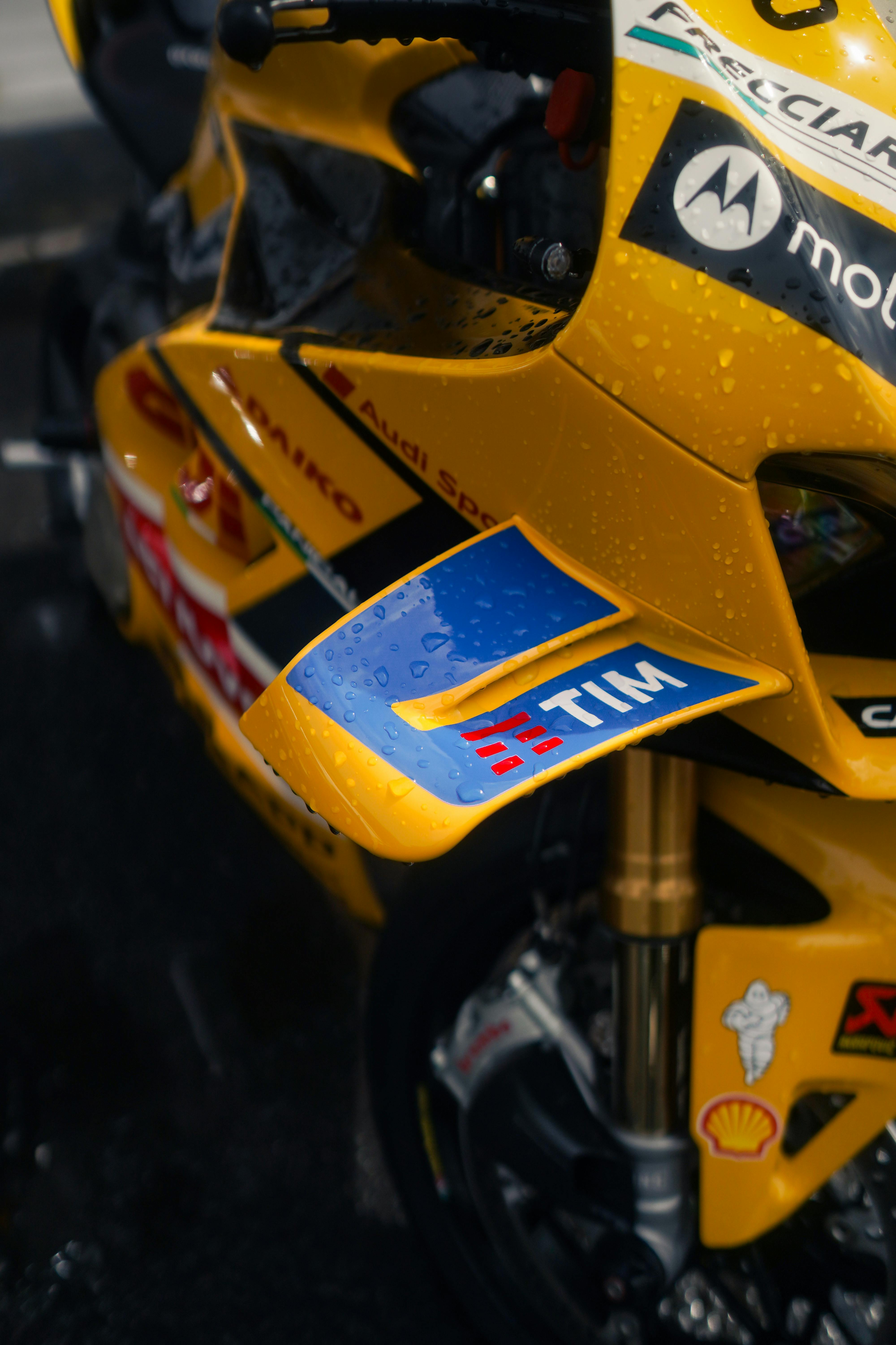 Detailed view of a yellow racing motorcycle adorned with sponsors' logos and raindrops.