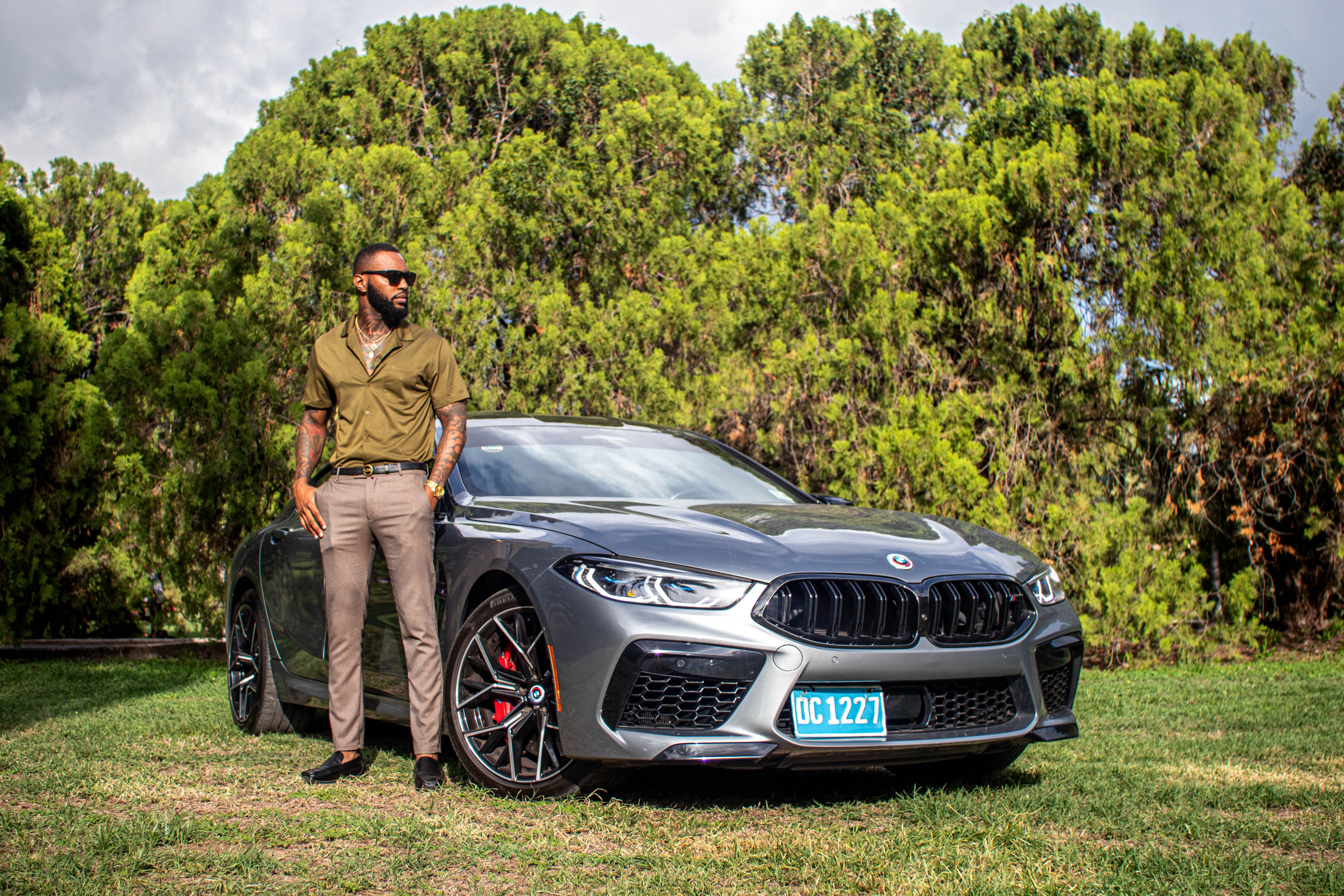 Man standing confidently beside a luxury car in a scenic outdoor setting.