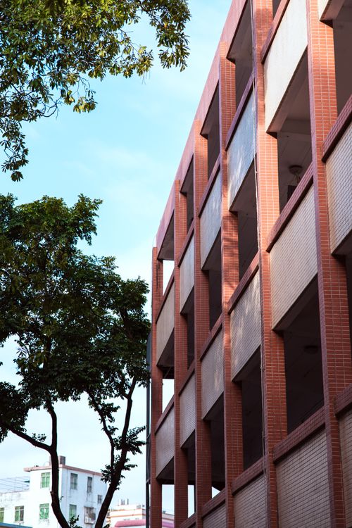 Free A modern brick building with open corridors against a clear blue sky, with trees in the foreground. Stock Photo