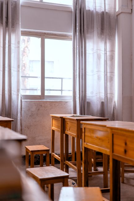 Miljöbild – A peaceful, empty classroom with sunlight streaming through the window onto wooden desks.