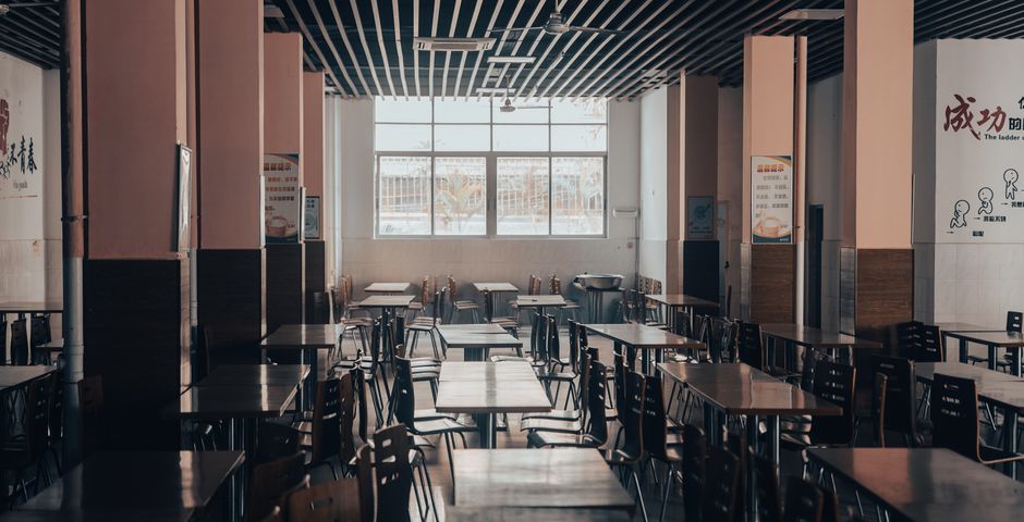 An empty school cafeteria with wooden tables — the canteen is the main indoor pest source