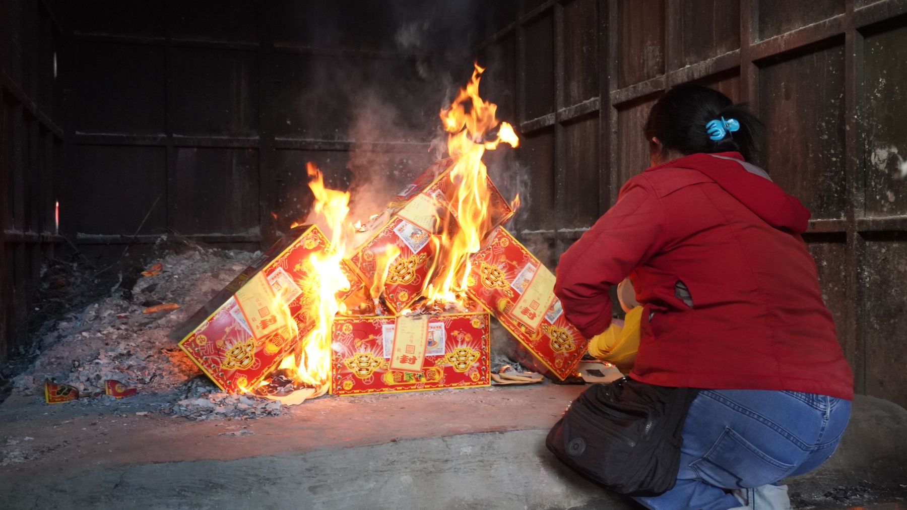 Indoor scene of a person performing a traditional Chinese joss paper burning ritual.
