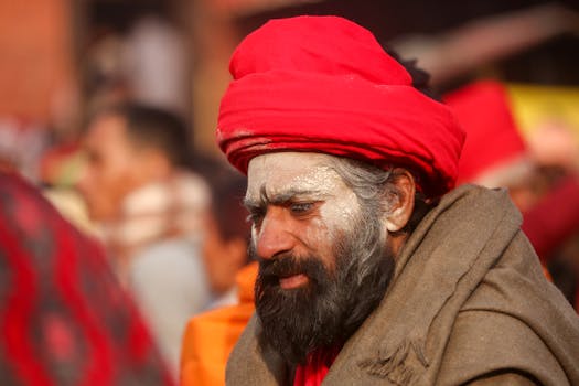 Candid shot of a Sadhu with a red turban and ash-covered face, captured outdoors during the day.
