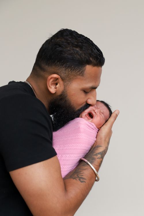 Free Loving father tenderly kisses his newborn baby swaddled in pink. Stock Photo