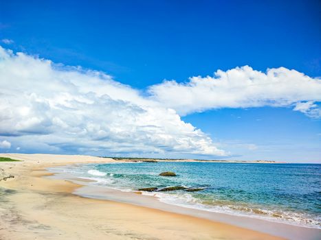 A serene sandy beach with clear blue skies and calm ocean waves, perfect for travel and relaxation.