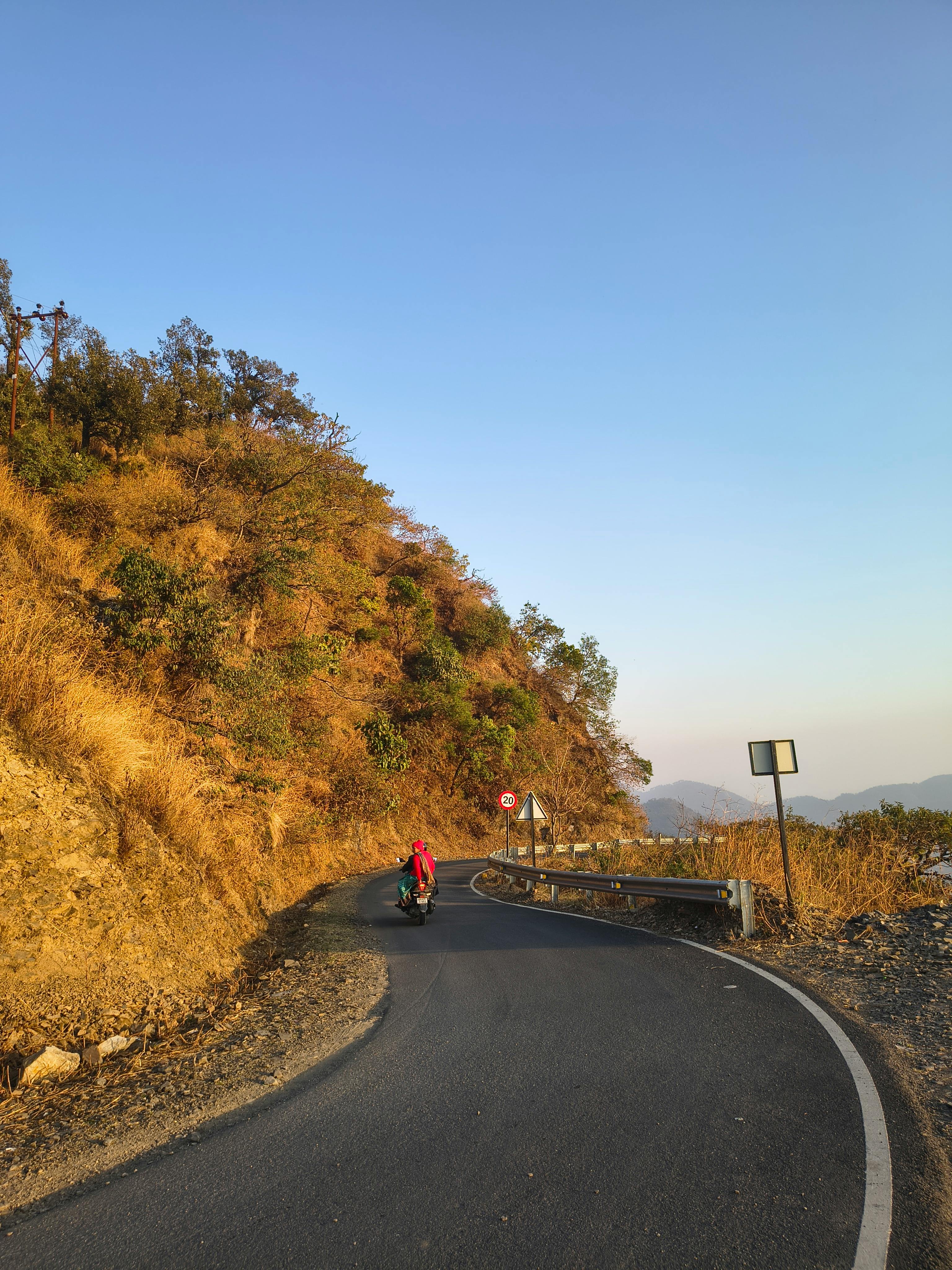 A lone motorcycle rides on a winding mountain road during sunset.