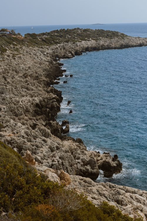 Free Stunning rocky coastline meeting the blue ocean under a clear sky, perfect for coastal and nature themes. Stock Photo