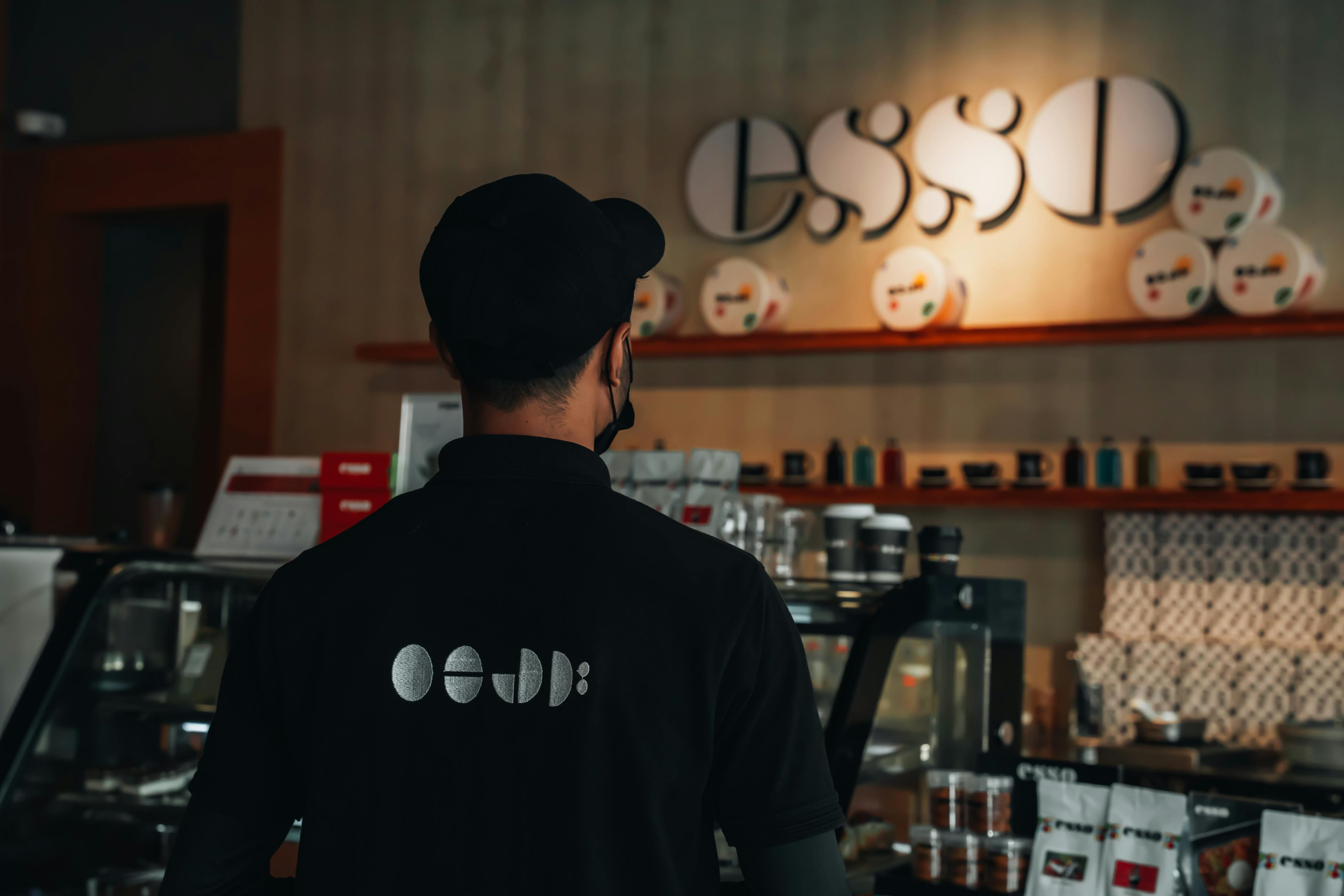 Miễn phí Một nhân viên pha chế trong một quán cà phê hiện đại với nội thất và biển hiệu trang trí bắt mắt, đang đứng đối diện quầy. Ảnh lưu trữ