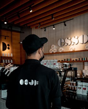 Barista wearing a black uniform inside a stylish coffee shop with warm lighting and modern design.