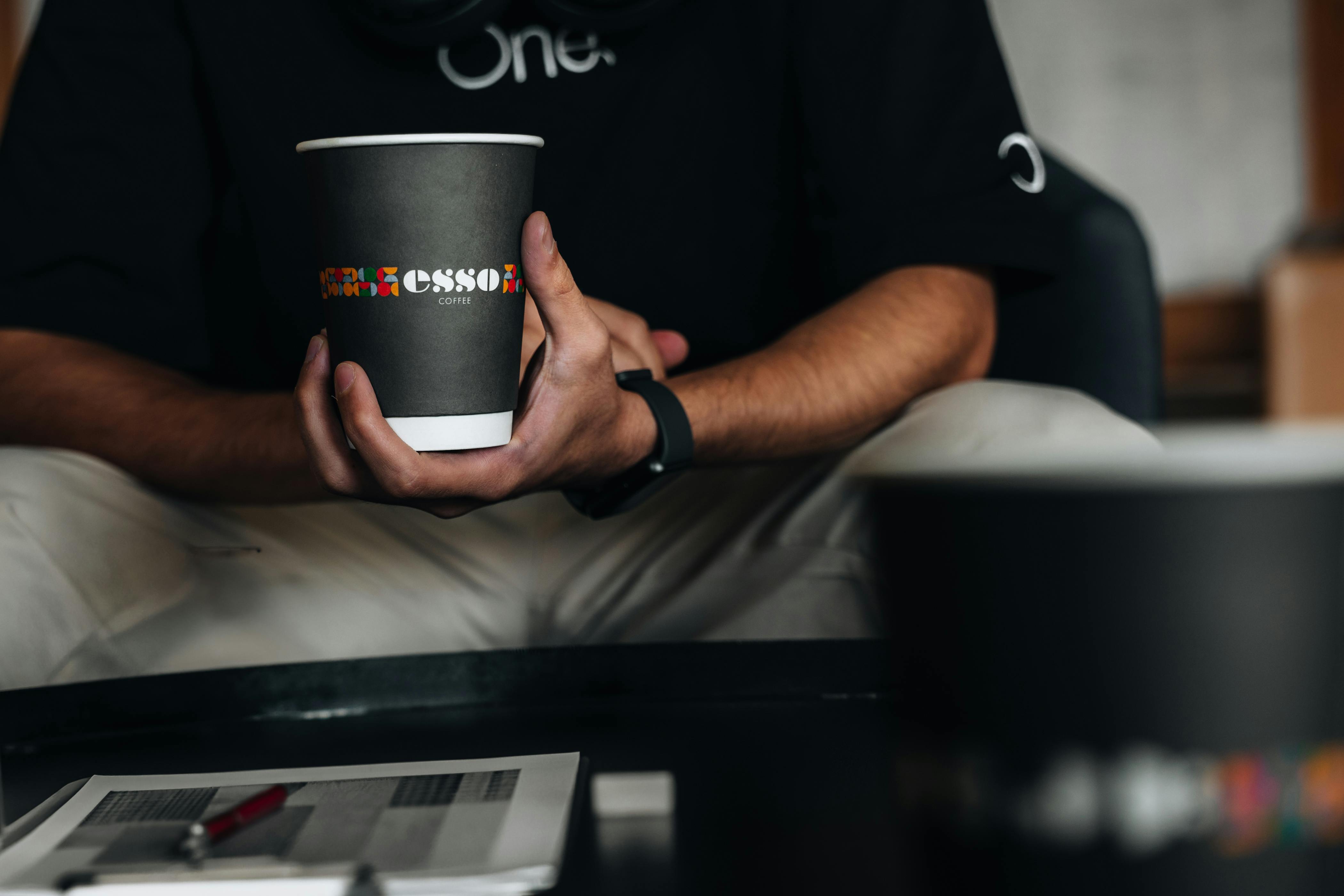 Gratis Primo piano di una persona che tiene in mano una tazza da caffè con un logo decorato in un ambiente rilassato. Foto a disposizione