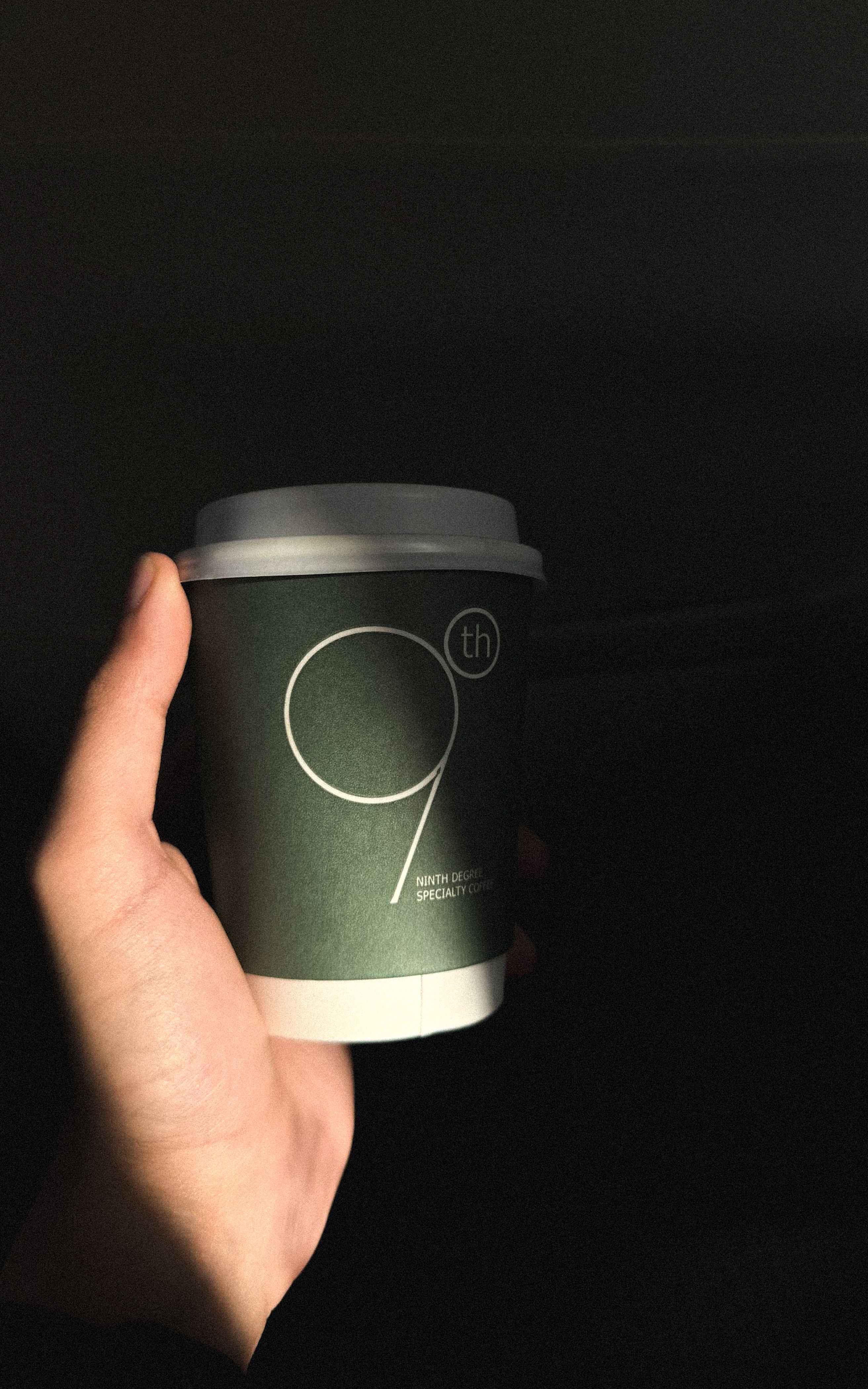 Close-up of a hand holding a stylish minimalist coffee cup against a dark background.