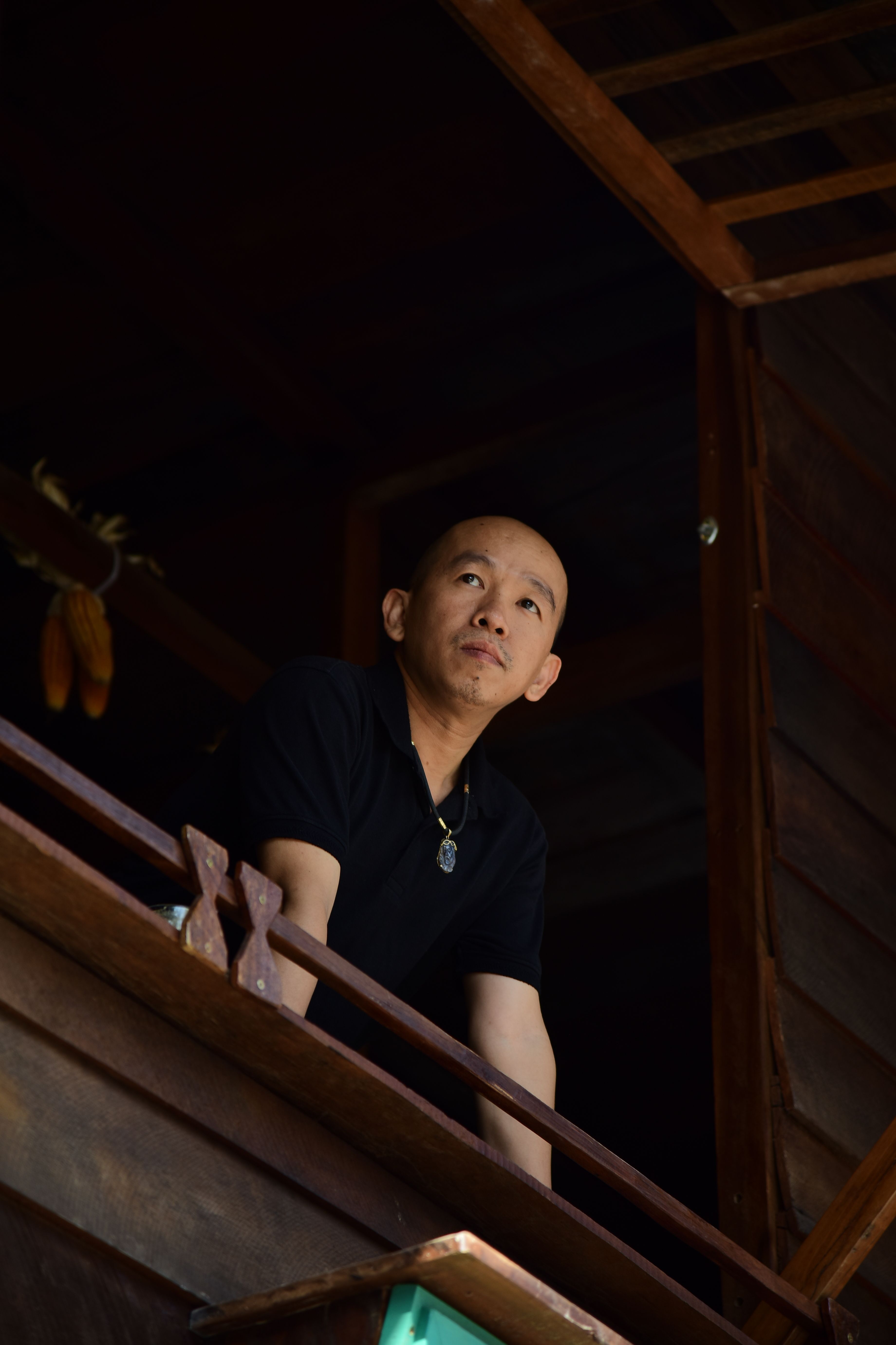 A man stands thoughtfully on a wooden balcony, gazing into the distance.