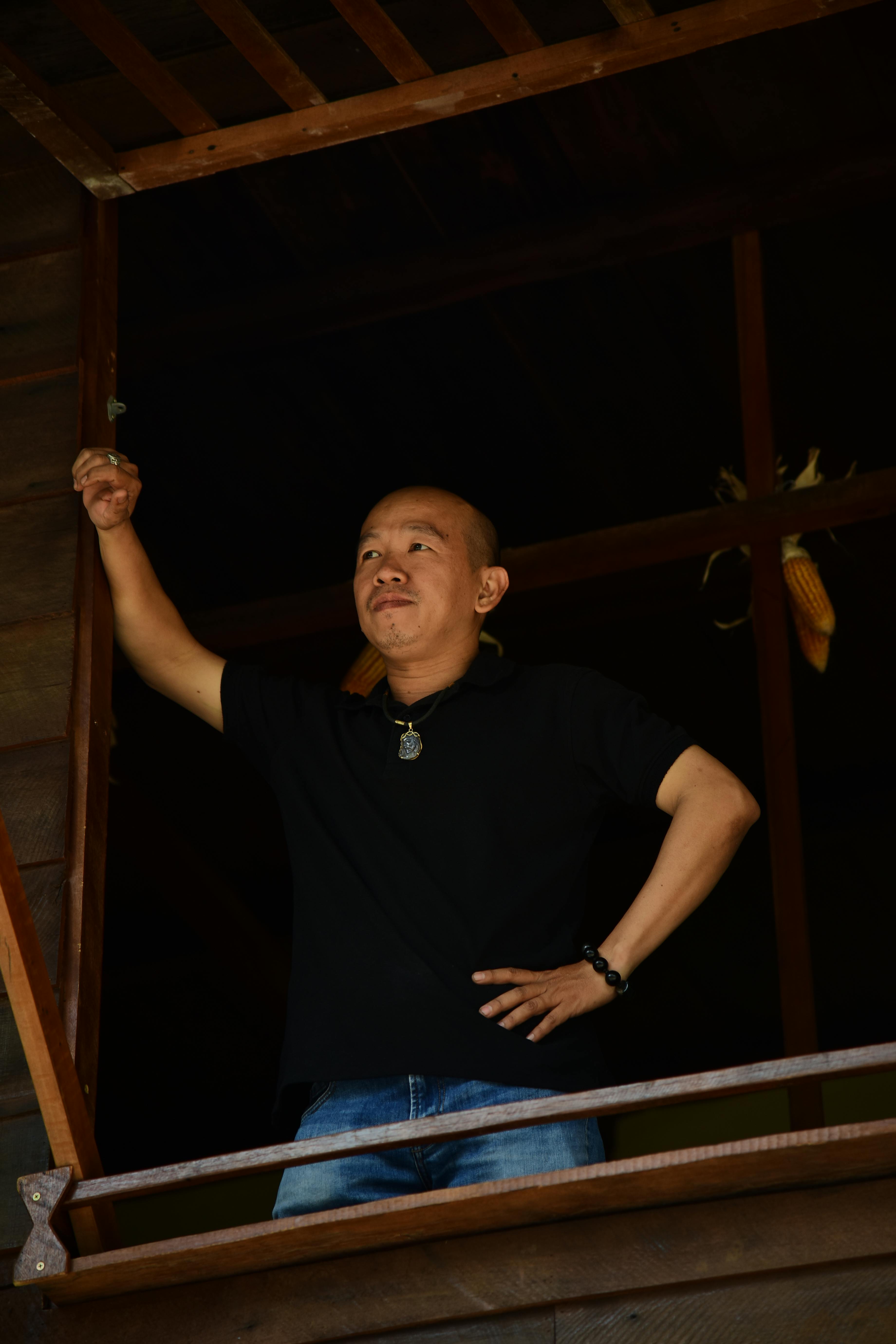 bezplatná Muž sebevědomě stojí uvnitř rustikální dřevěné budovy a dívá se ven. Základová fotografie