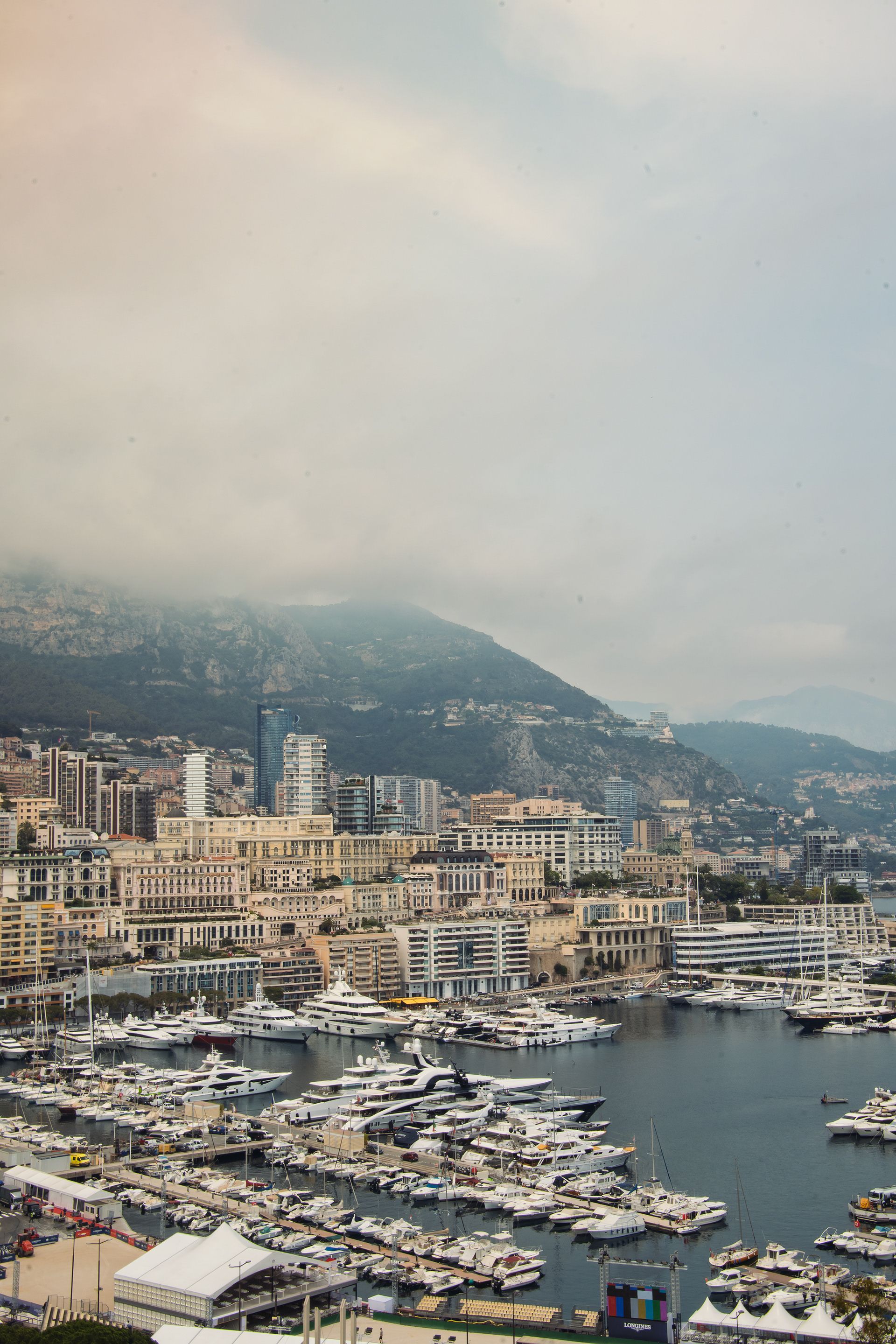 Scenic view of Monte Carlo harbor with luxurious yachts and cityscape against a mountainous backdrop.
