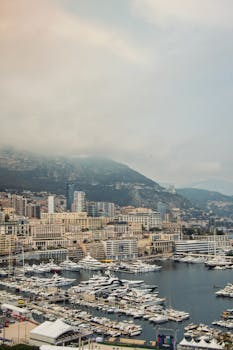 Scenic view of Monte Carlo harbor with luxurious yachts and cityscape against a mountainous backdrop.