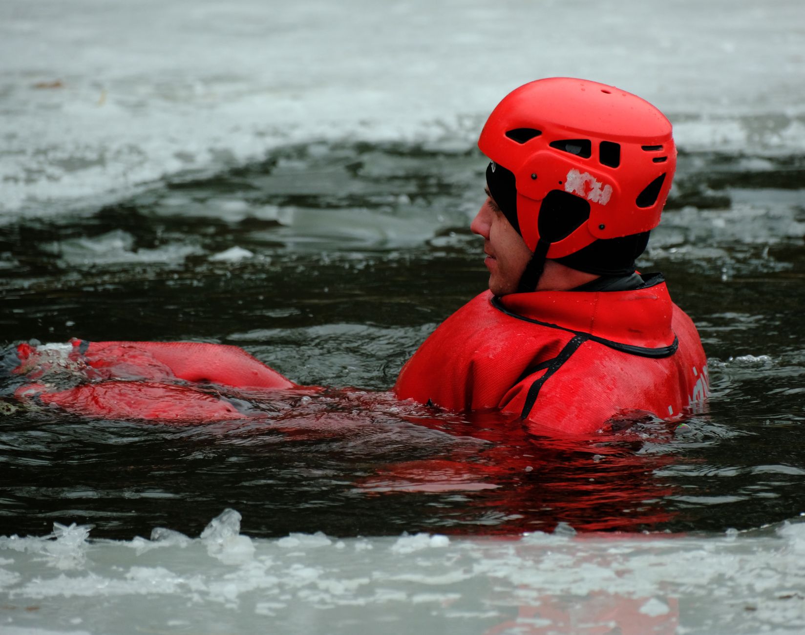 Man in bright gear practices winter ice rescue in icy waters.