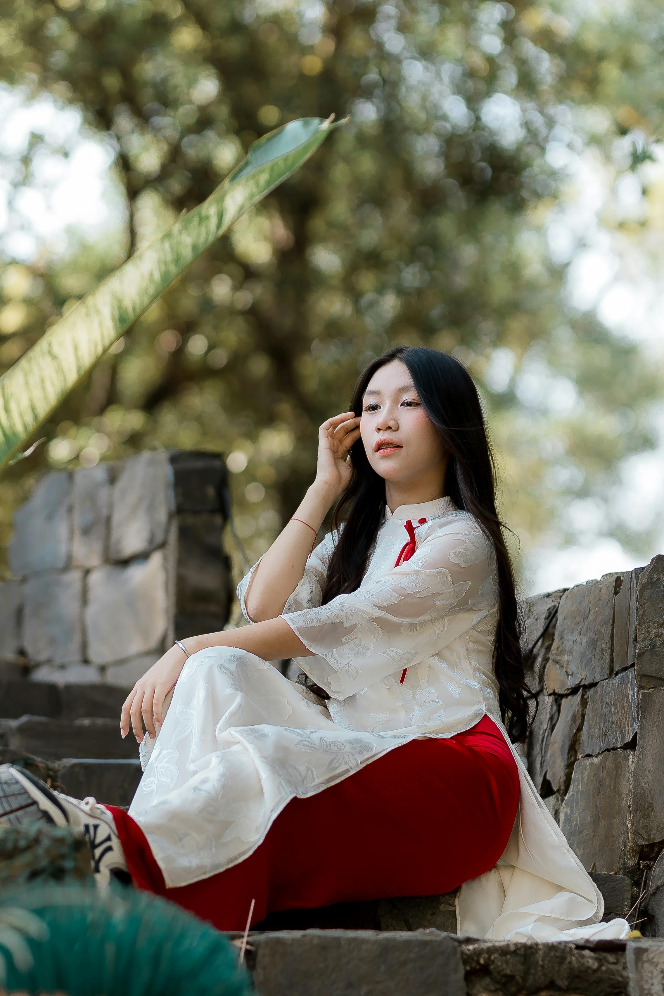 ฟรี หญิงสาวสวมชุดพื้นเมืองนั่งอยู่บนบันไดหินที่ล้อมรอบด้วยพืชพรรณเขียวชอุ่ม คลังภาพถ่าย