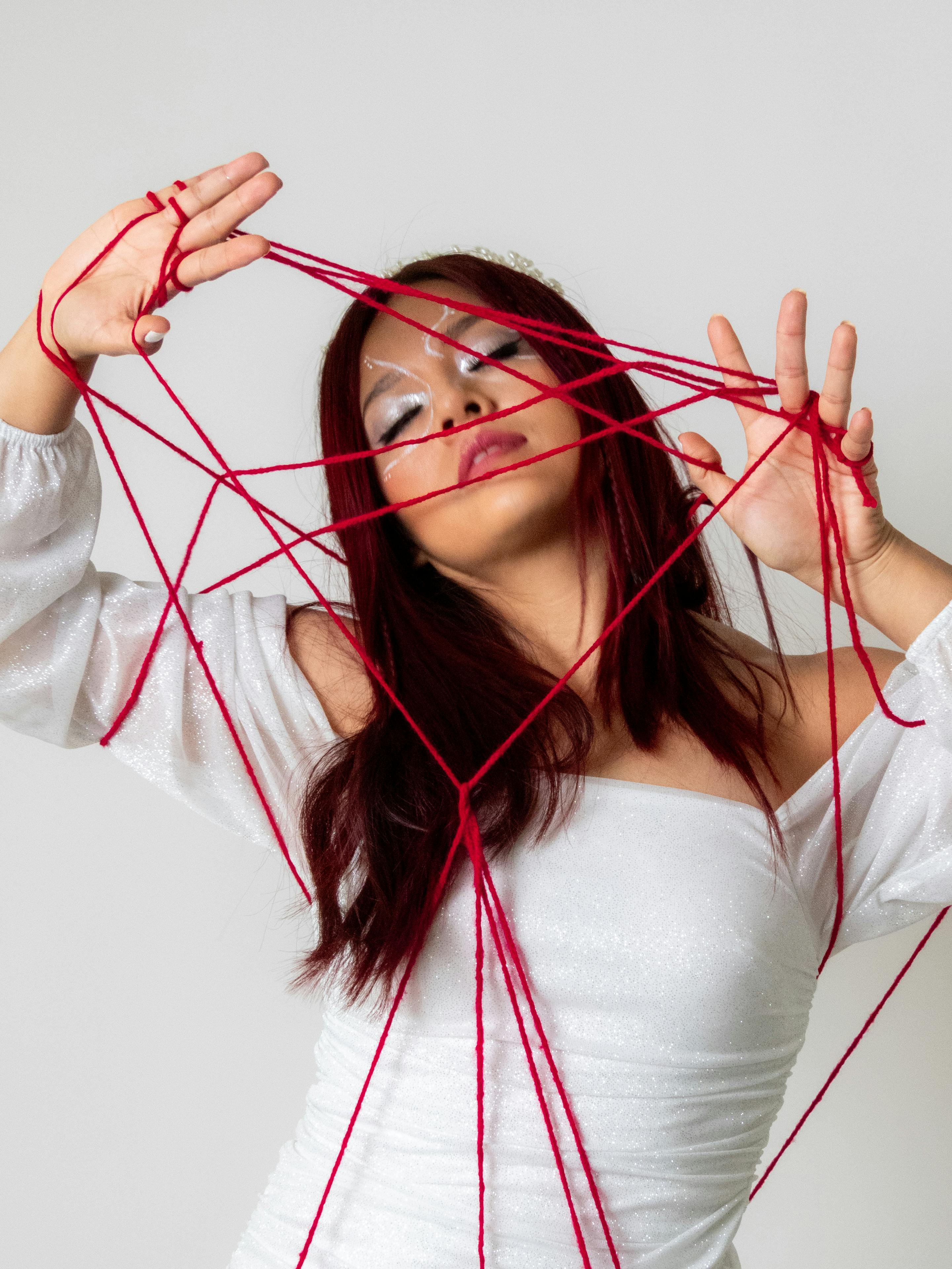 Free Artistic portrait of a woman entangled in red yarn threads against a minimalist background. Stock Photo
