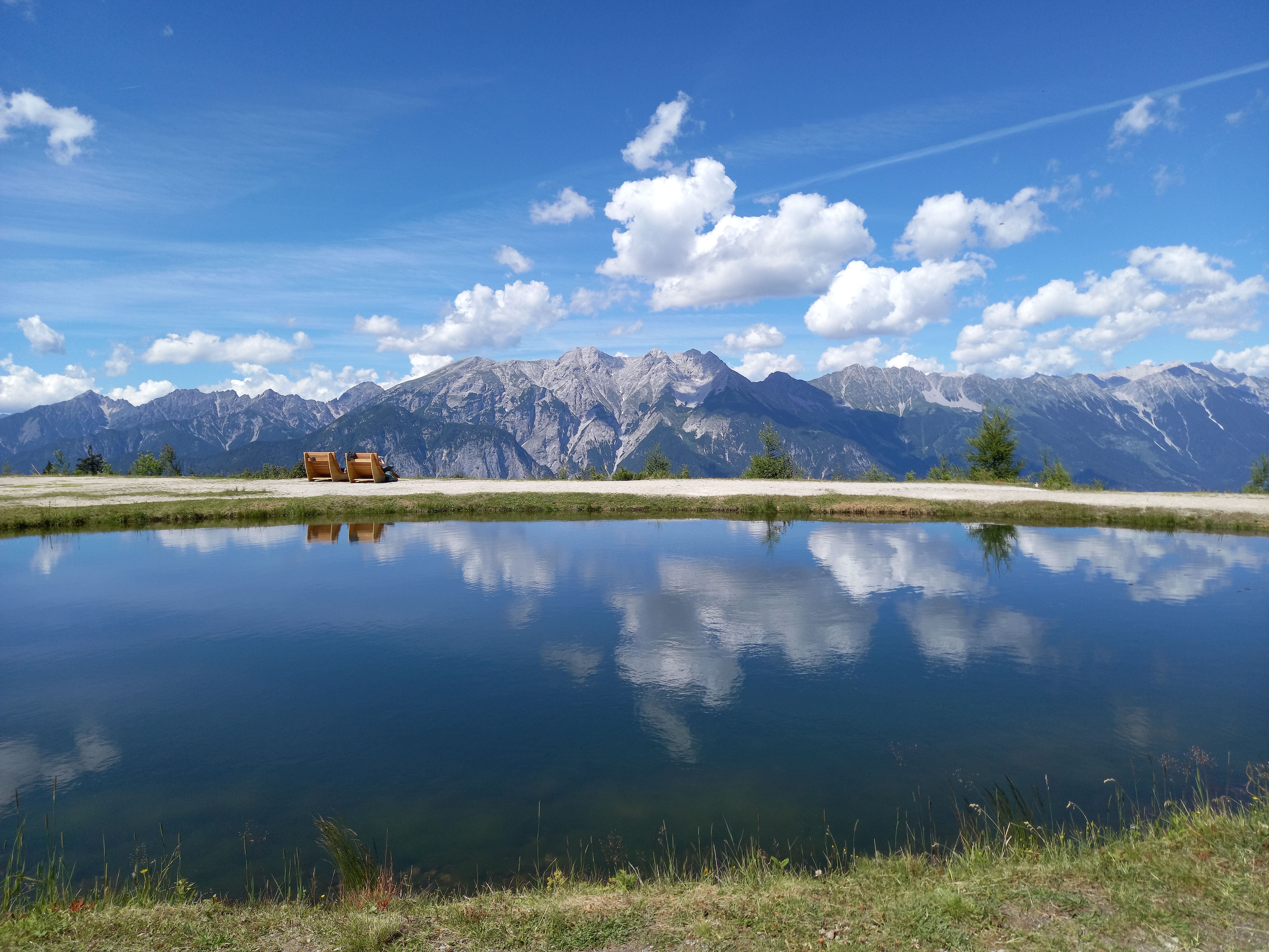 Breathtaking view of the Stubaier Alpen with a serene reflective lake under a bright blue sky.