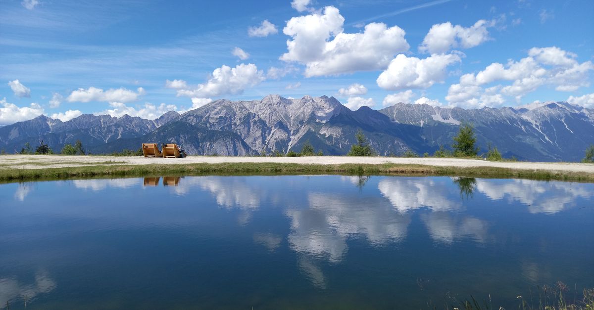 Breathtaking view of the Stubaier Alpen with a serene reflective lake under a bright blue sky.