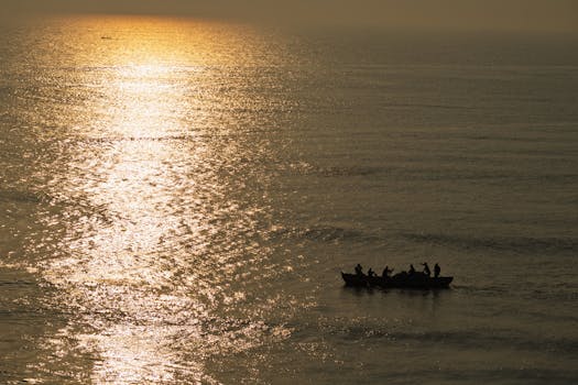 A fishing boat silhouetted against a serene sunset on the ocean, reflecting golden light.