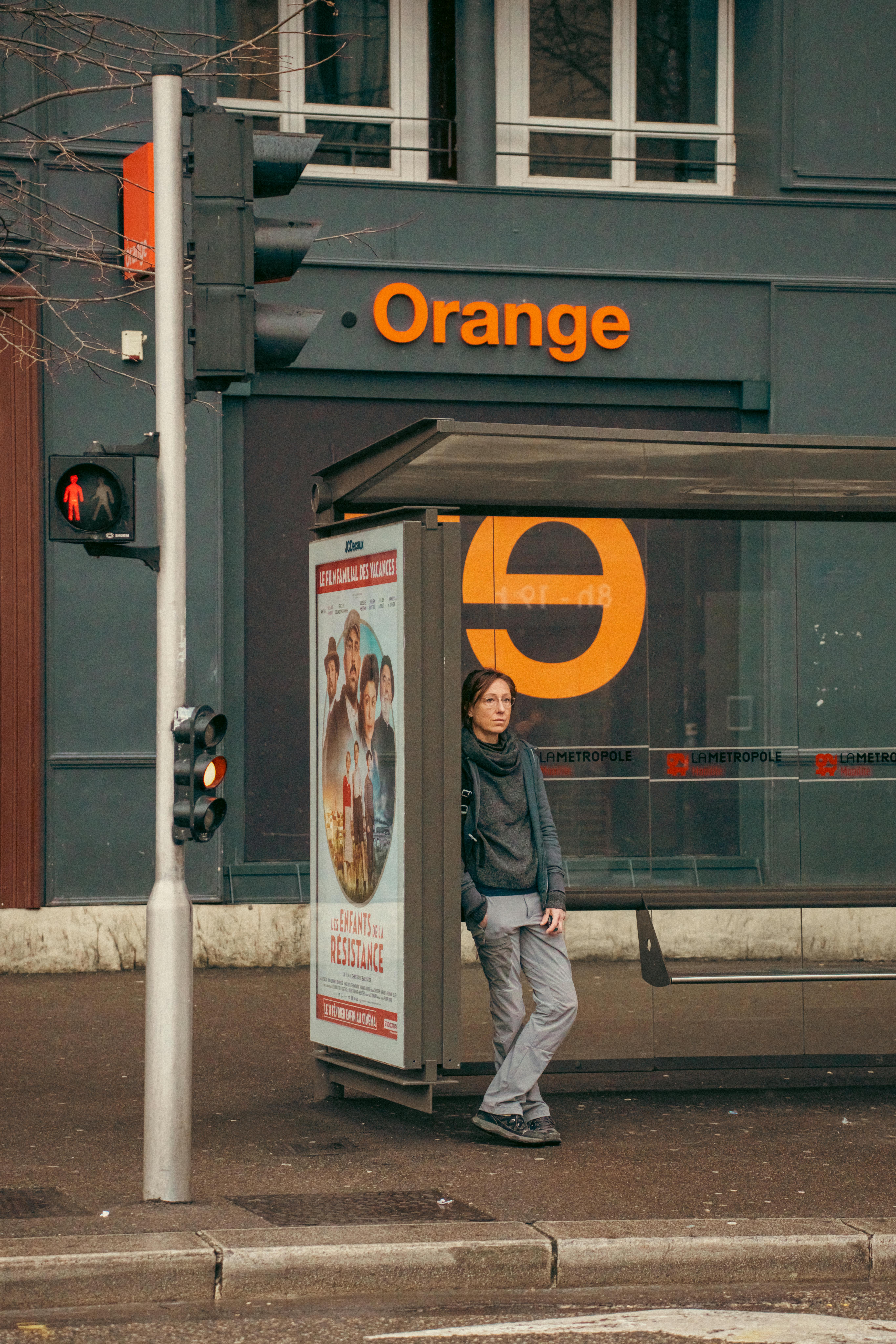 Gratis Seseorang menunggu di halte bus di luar toko Orange di Prancis, mengabadikan kehidupan sehari-hari di perkotaan. Foto Stok