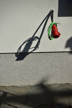Close-up of a red electrical cable casting a shadow on a wall.