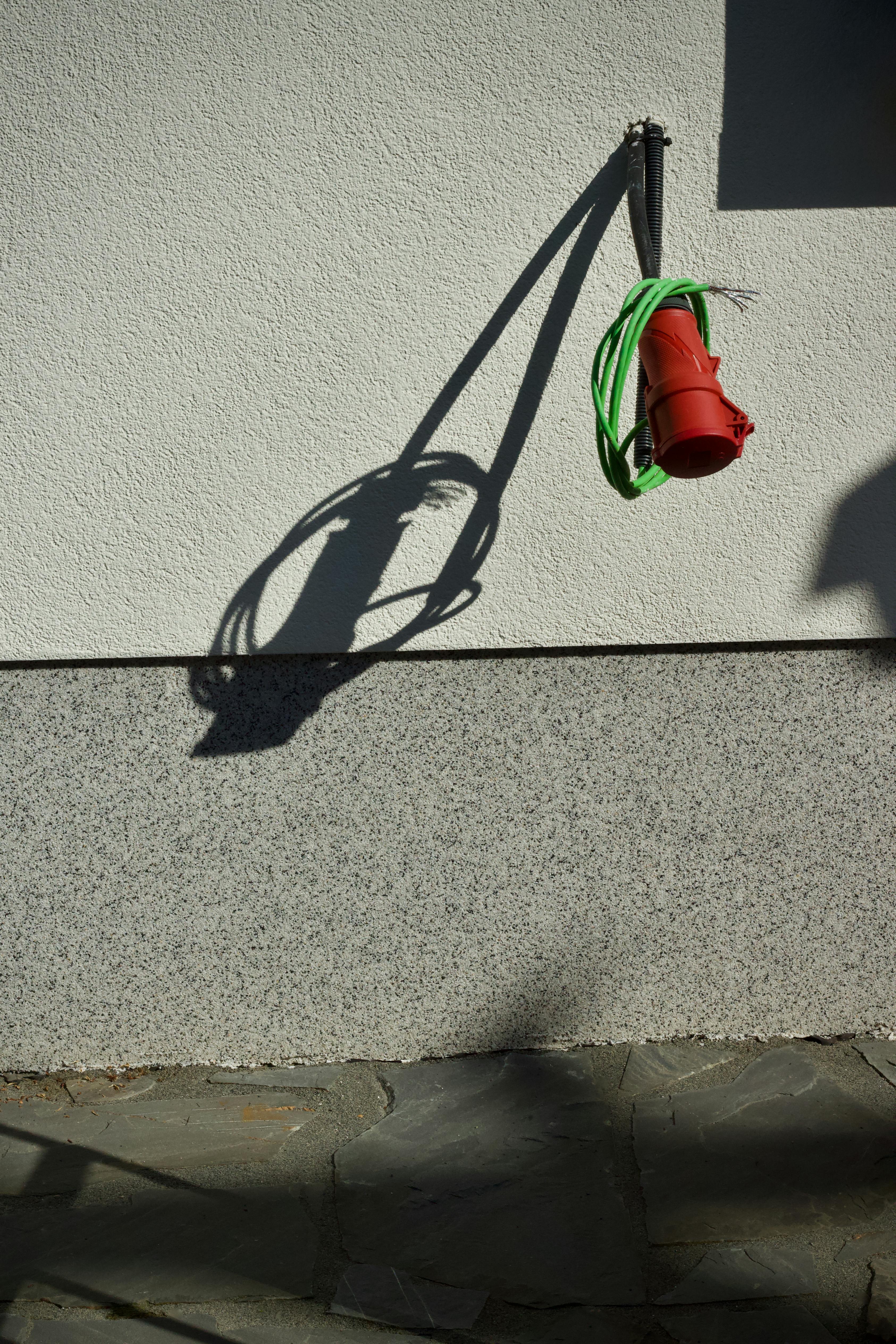 Gratis Primo piano di un cavo elettrico rosso che proietta un'ombra su un muro. Foto a disposizione
