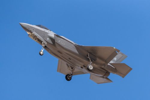 Free F35 fighter jet in flight with landing gear visible against clear blue sky, showcasing military aviation prowess. Stock Photo