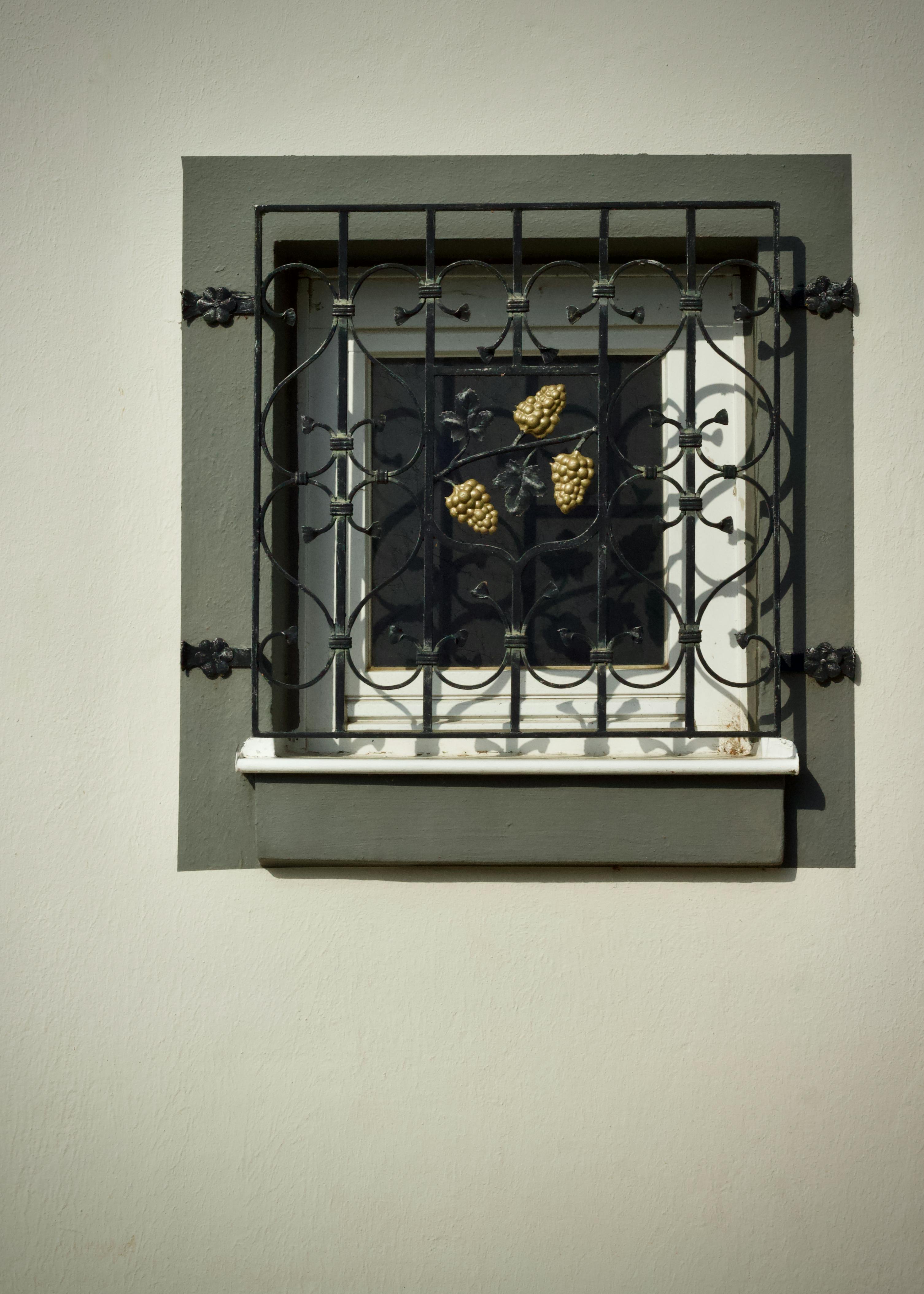 Gratis En dekorativ vinduesrist af jern med druemotiver på en malet bygningsvæg. Lagerfoto