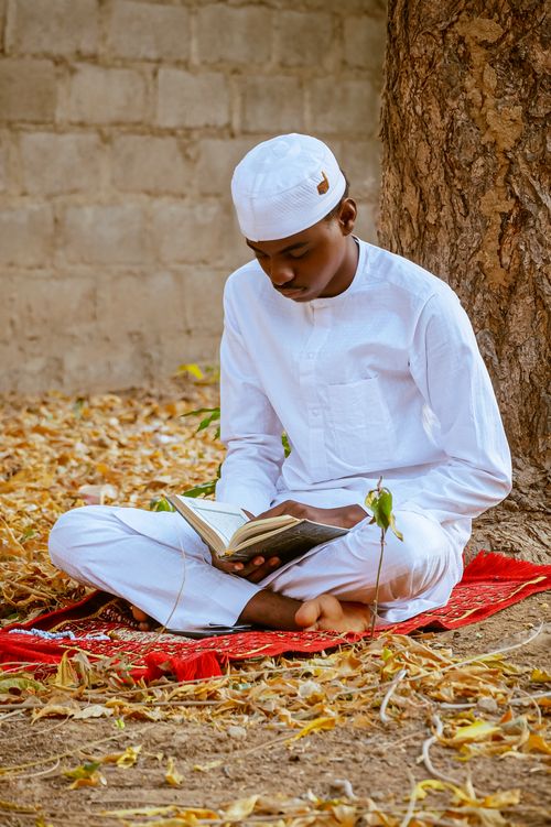 Free A young man in traditional clothing reads a holy book outdoors, surrounded by autumn leaves. Stock Photo