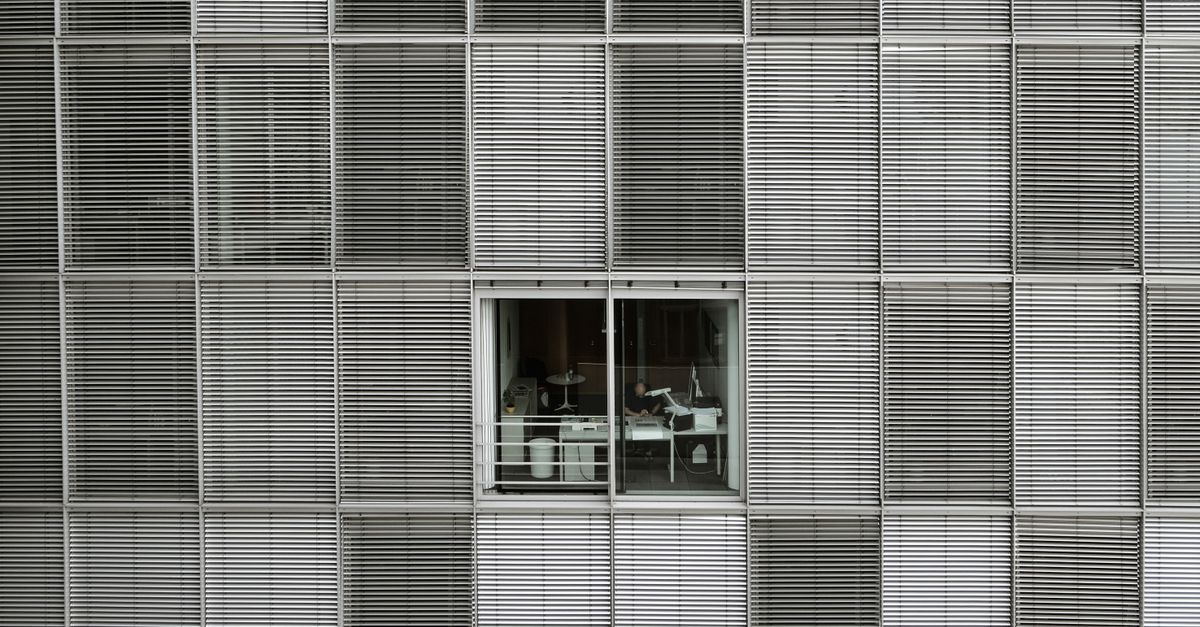 Fachada exterior de edificio moderno con ventana que revela un interior de oficina.
