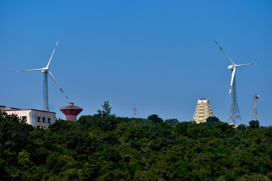 Scenic view of wind turbines and ancient temple amidst lush greenery under clear blue skies in Nellore, India.