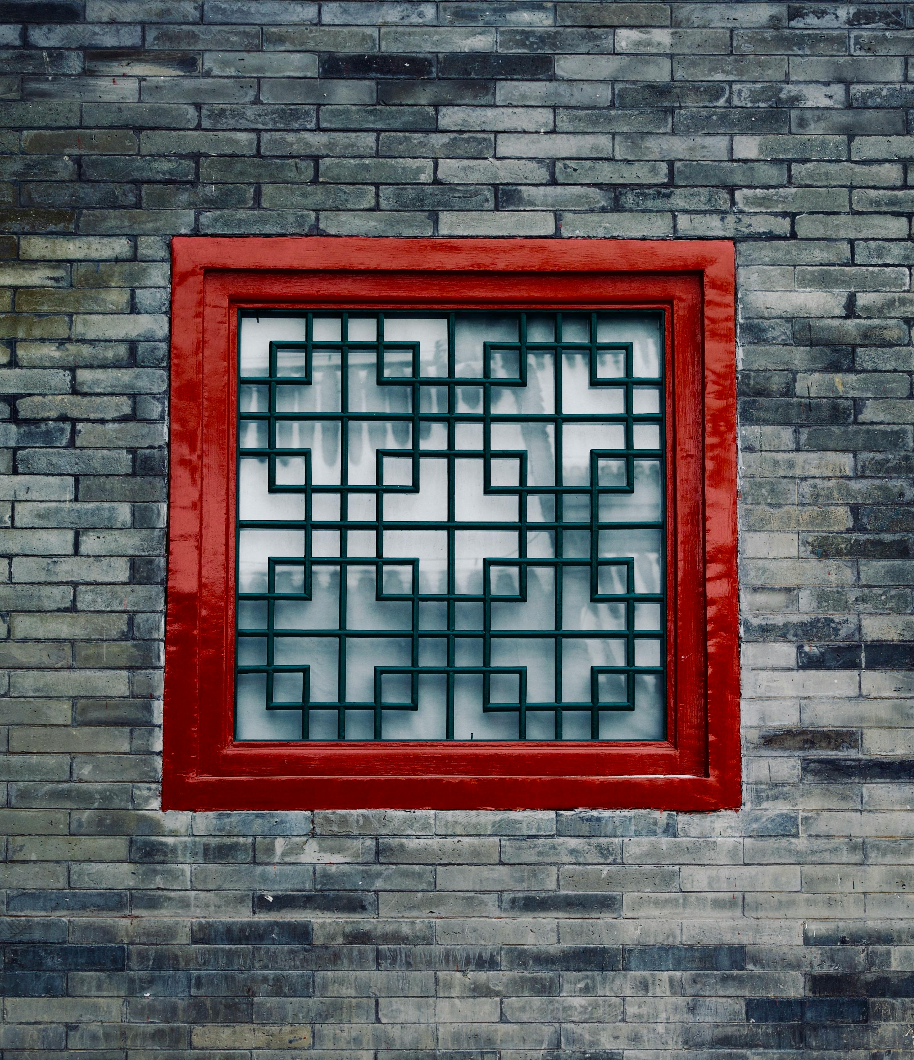 Gratuit Une fenêtre à cadre rouge et à motif géométrique, encastrée dans un mur de briques grises. Photos