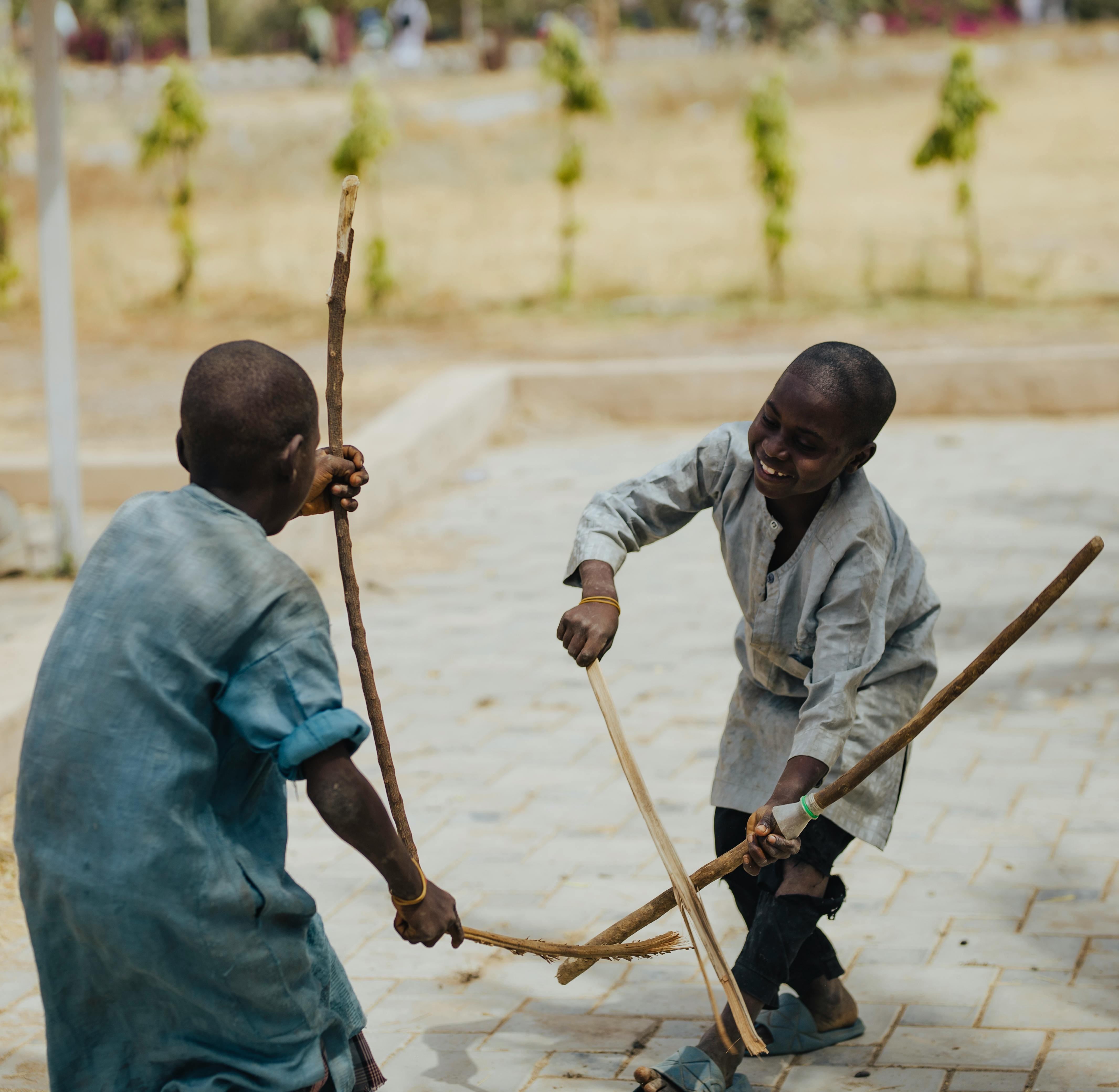 Two children playfully engage in a stick game outdoors, showcasing joy and energy.