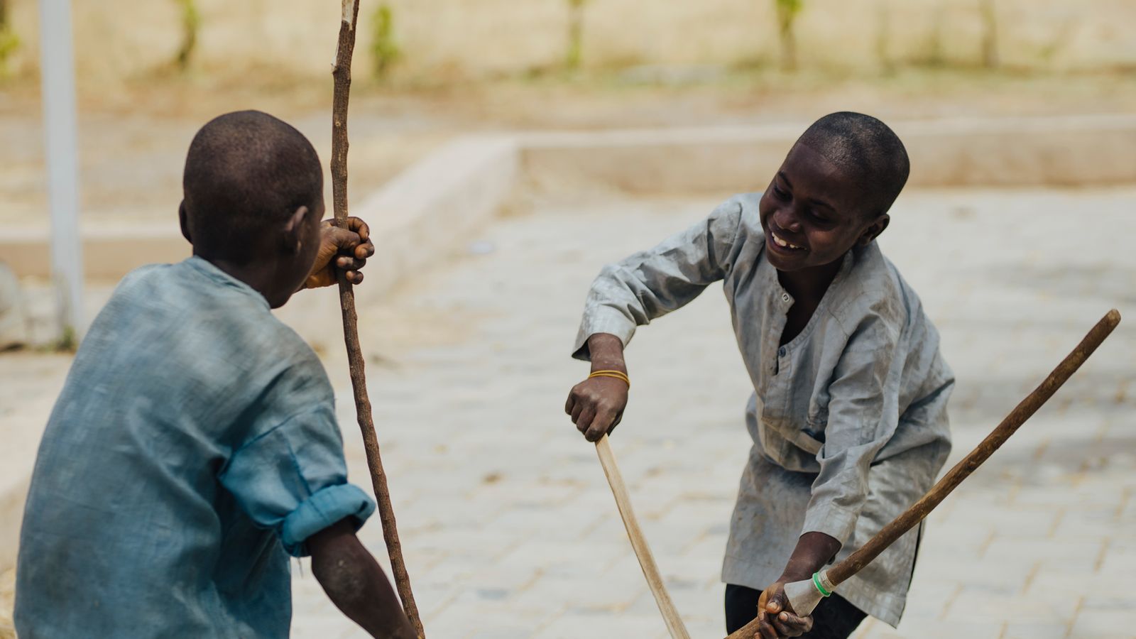 Two children playfully engage in a stick game outdoors