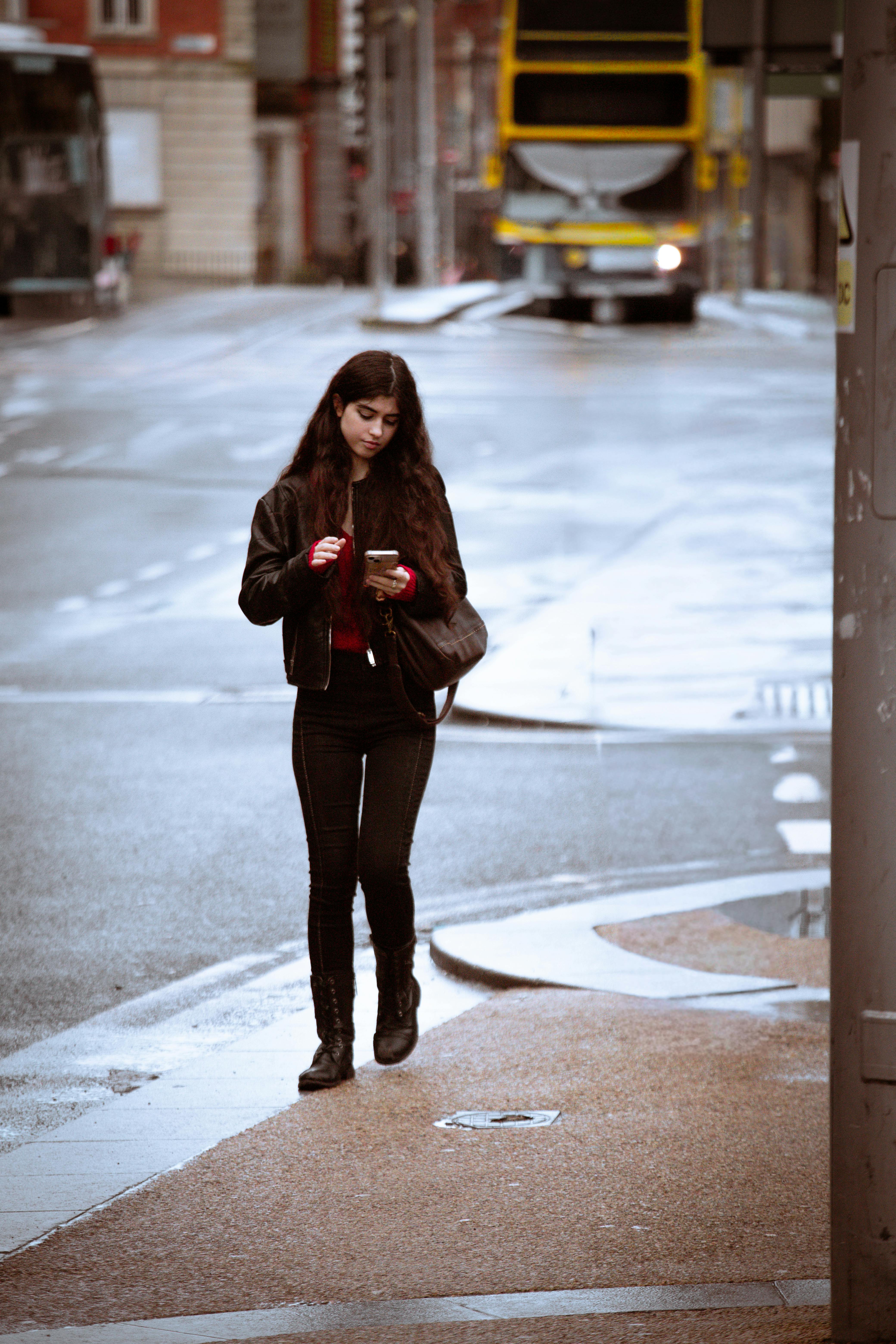 Gratis Una giovane donna con una giacca di pelle usa il suo telefono mentre cammina in una strada piovosa a Dublino, in Irlanda. Foto a disposizione