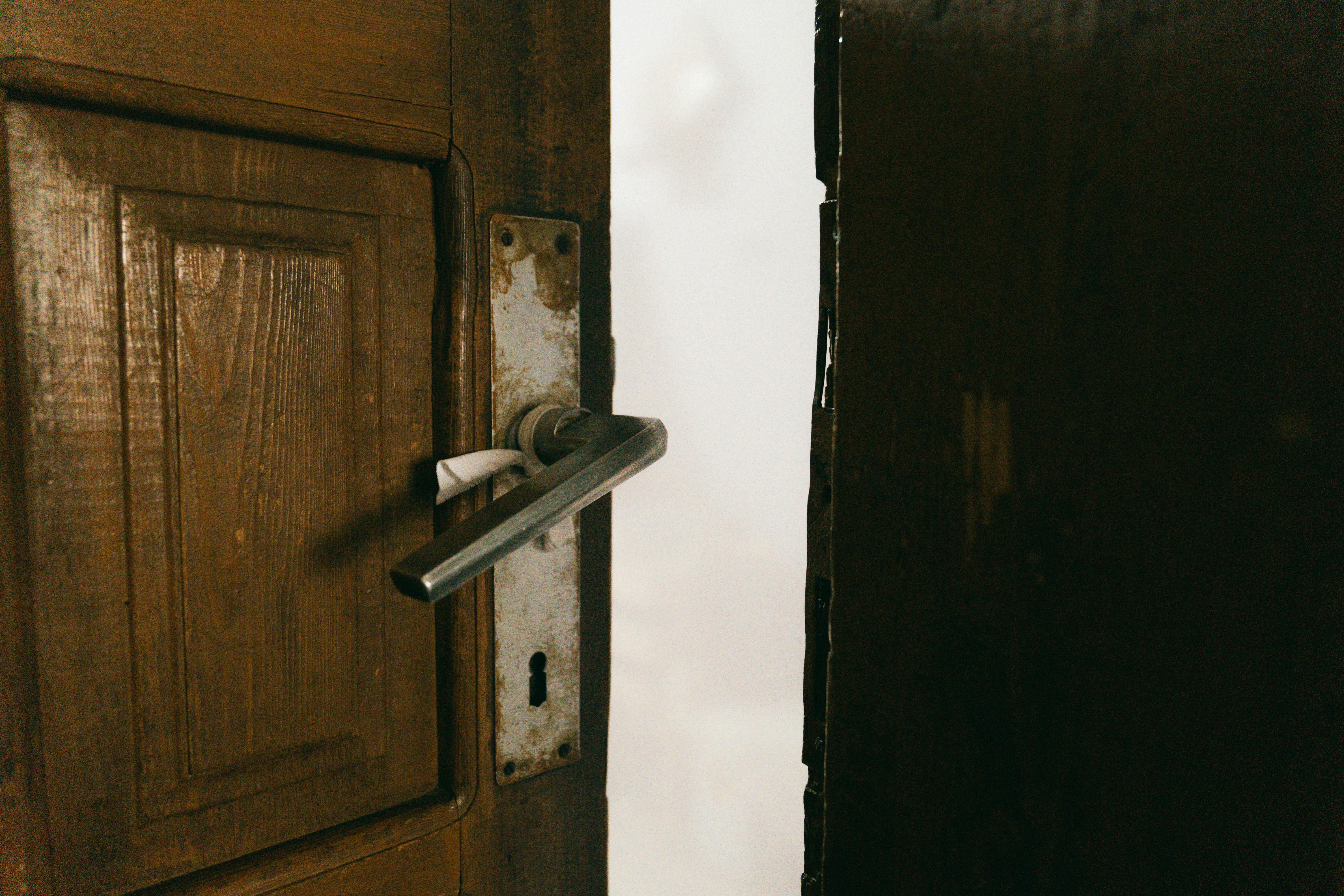 Gratis Una puerta rústica de madera ligeramente entreabierta con una manija de metal, creando un ambiente misterioso. Foto de stock