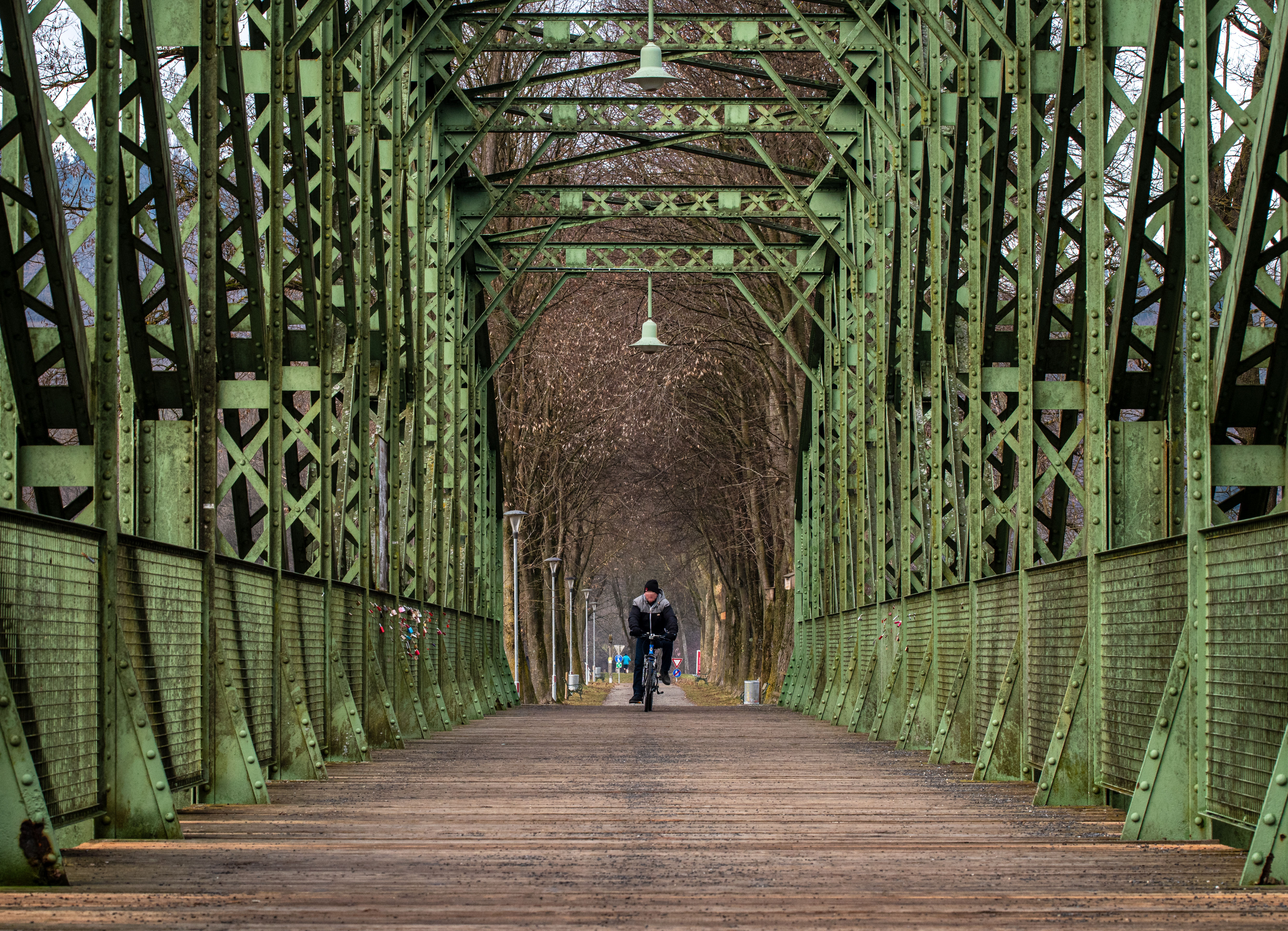 A person rides a bicycle across a picturesque green steel bridge surrounded by trees.