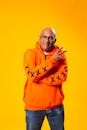 一位开朗的男人，身穿橙色连帽衫，在亮黄色背景下自信地摆着姿势