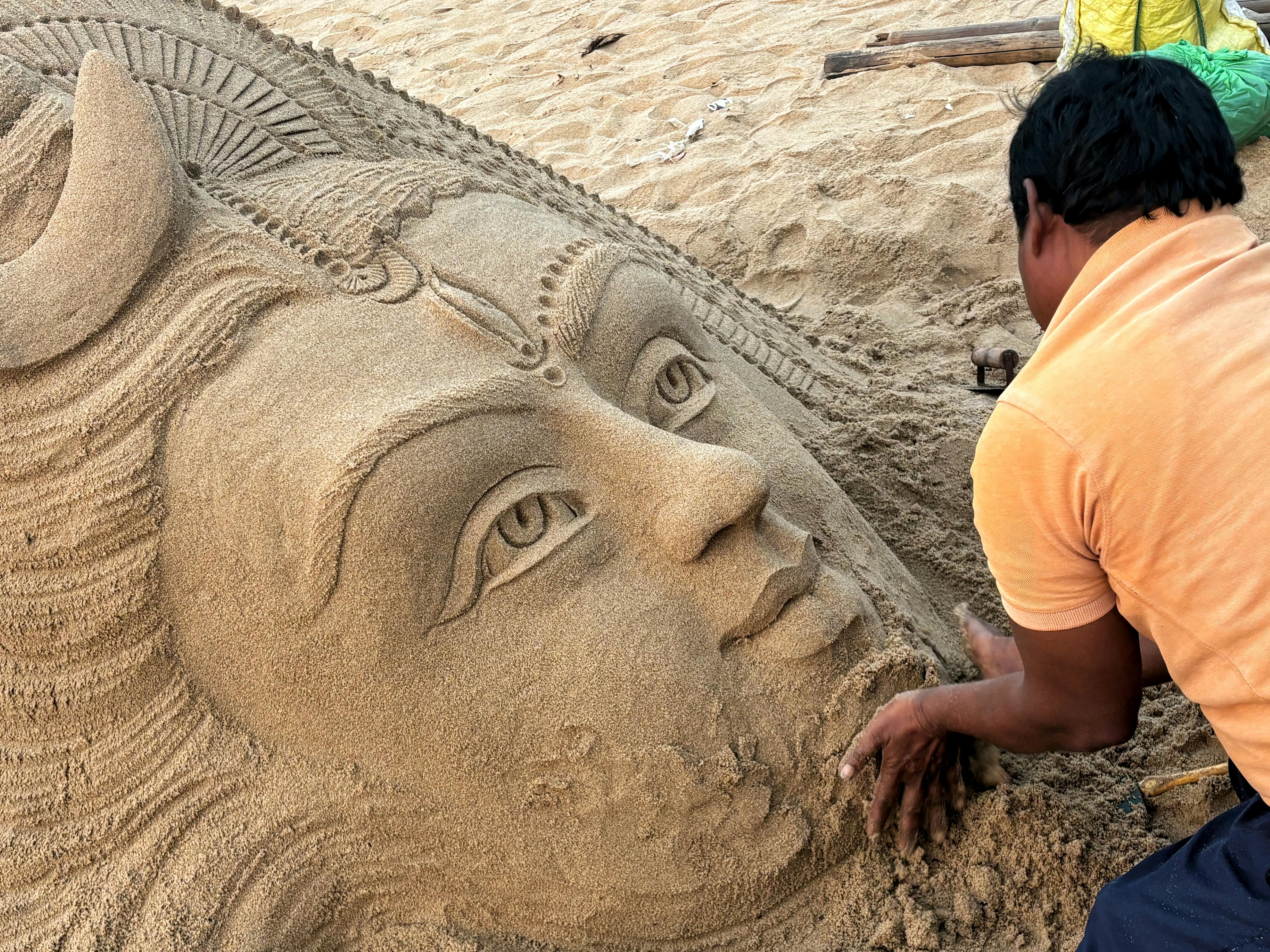 Artist meticulously crafting a detailed sand sculpture of a deity on Puri Beach, India.