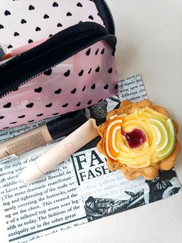 A pastry and cosmetic bag with makeup on a fashion-themed background.