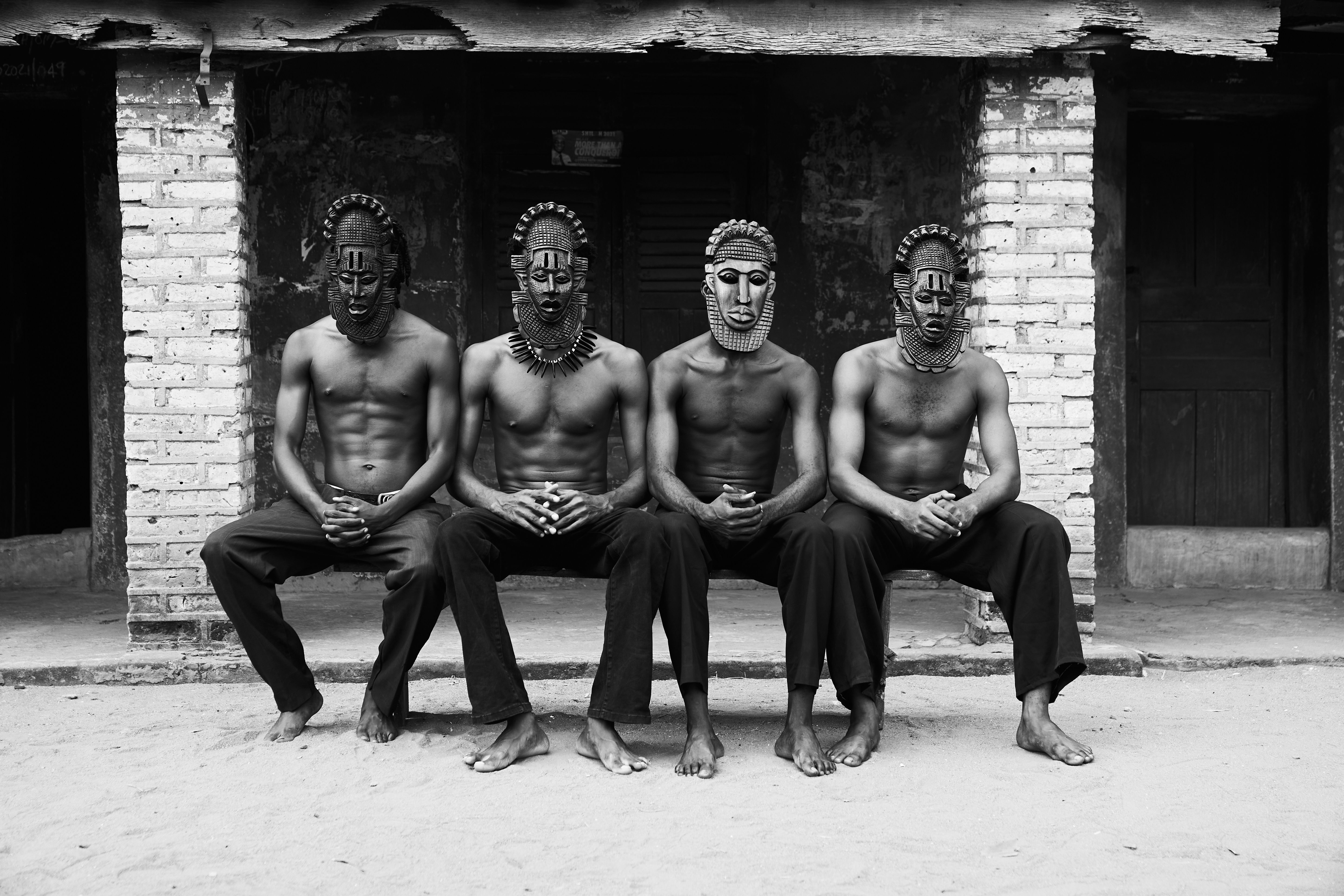 Four men with traditional masks sit in unity, showcasing cultural heritage.