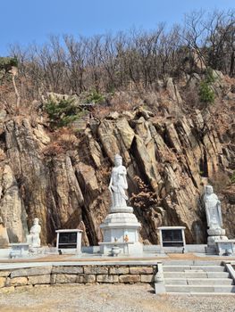 Outdoor Buddhist statues against rocky cliffs under clear skies, evoking a serene and spiritual ambiance.