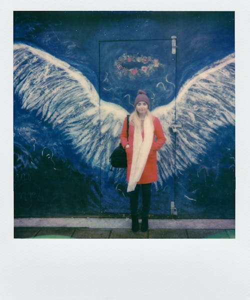 Woman in Orange Coat Standing in Front of Angel Wings