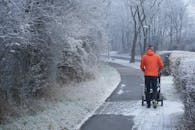 白天，一名身穿红色夹克的男子推着婴儿车，沿着维也纳一条霜冻的人行道前行