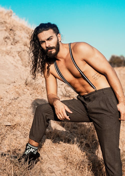 A Shirtless Man With Long Hair Wearing Suspender Outdoors
