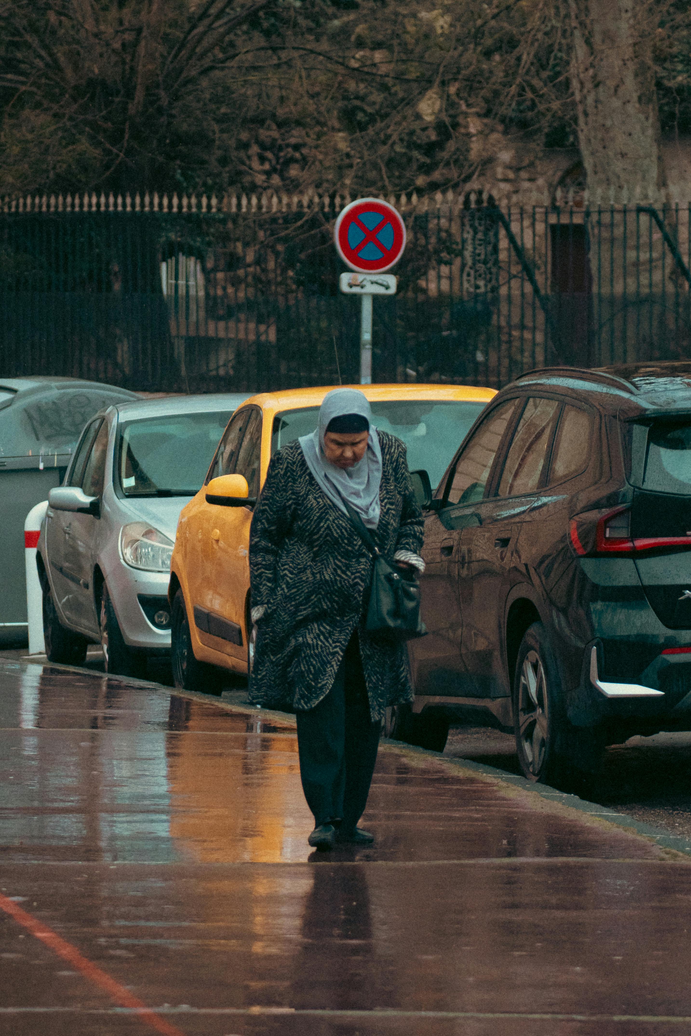 common:alt.prefix Iäkäs nainen kävelee pysäköityjen autojen ohi sateisena päivänä Marseillessa, Ranskassa. common:alt.postfix