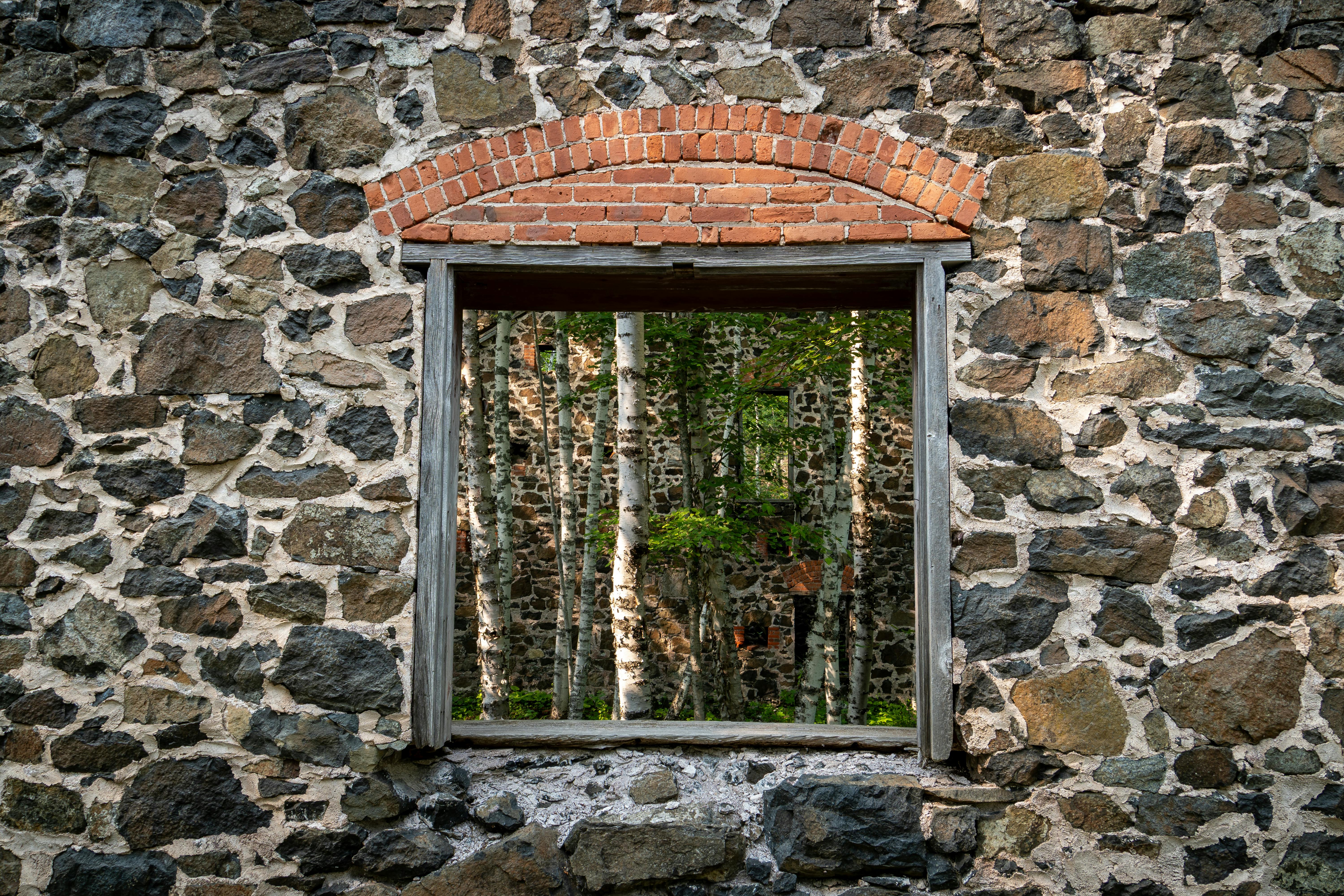Kostenlos Ein Fensterrahmen in einer Steinmauer gibt den Blick auf Birken frei, die in einer alten Bergwerksruine in Michigan wachsen. Stock-Foto