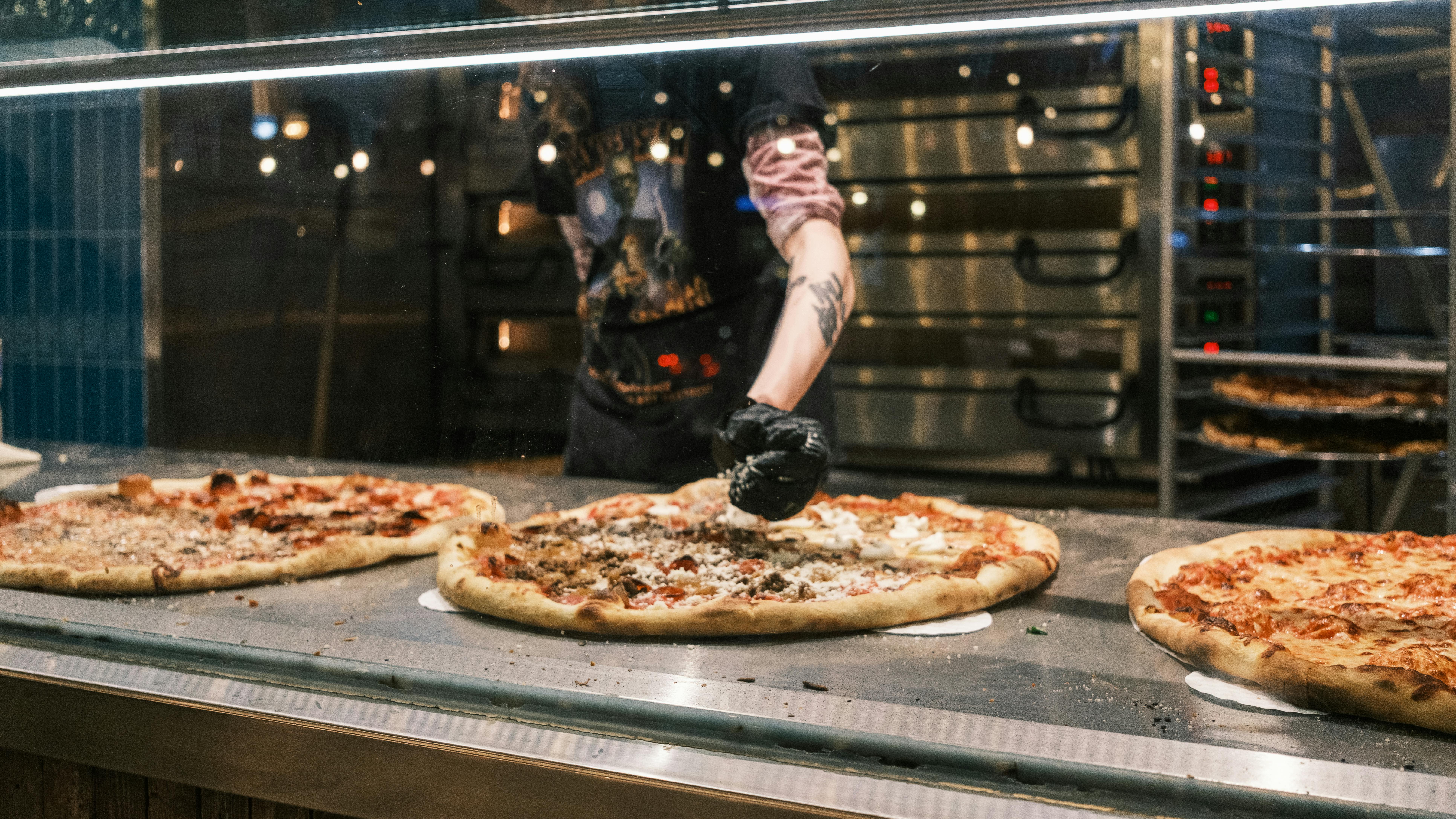 Chef garnishes pizzas in a vibrant pizzeria with ample copyspace and a focus on artisanal quality.